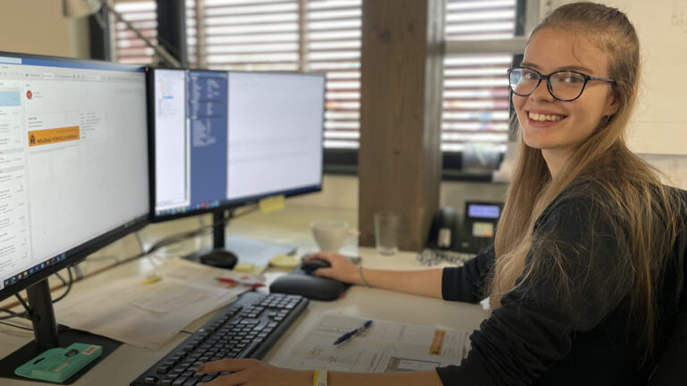 Bauzeichner-Azubine Lissi an ihrem Arbeitsplatz hinter zwei Bildschirmen